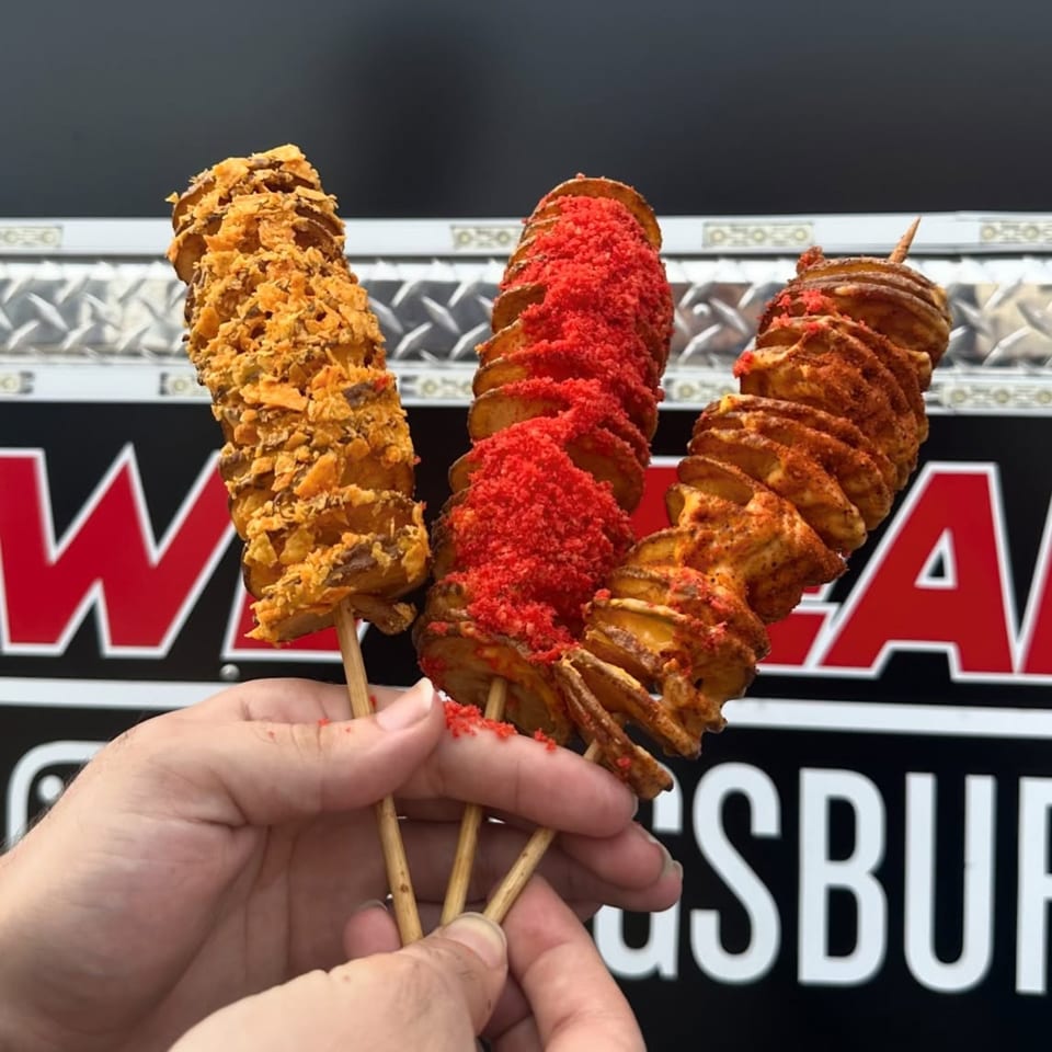 Three tornado potato skewers, one with crushed chips, one with red seasoning, and one with chili powder.