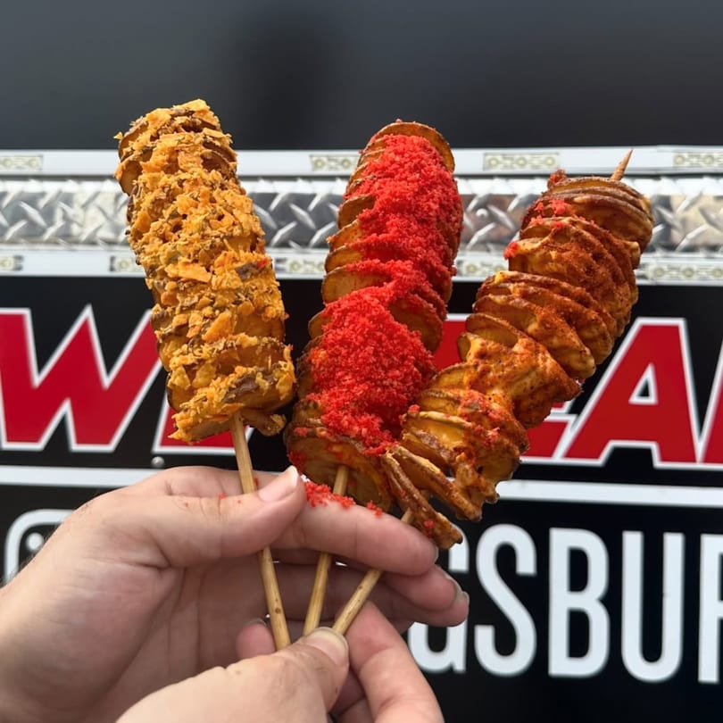Three tornado potato skewers, one with crushed chips, one with red seasoning, and one with chili powder.